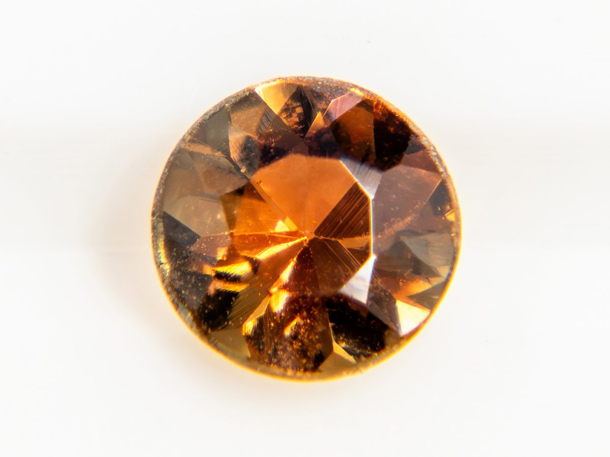 Close-up of a small round faceted amber-coloured transparent stone on a white background — sample photo